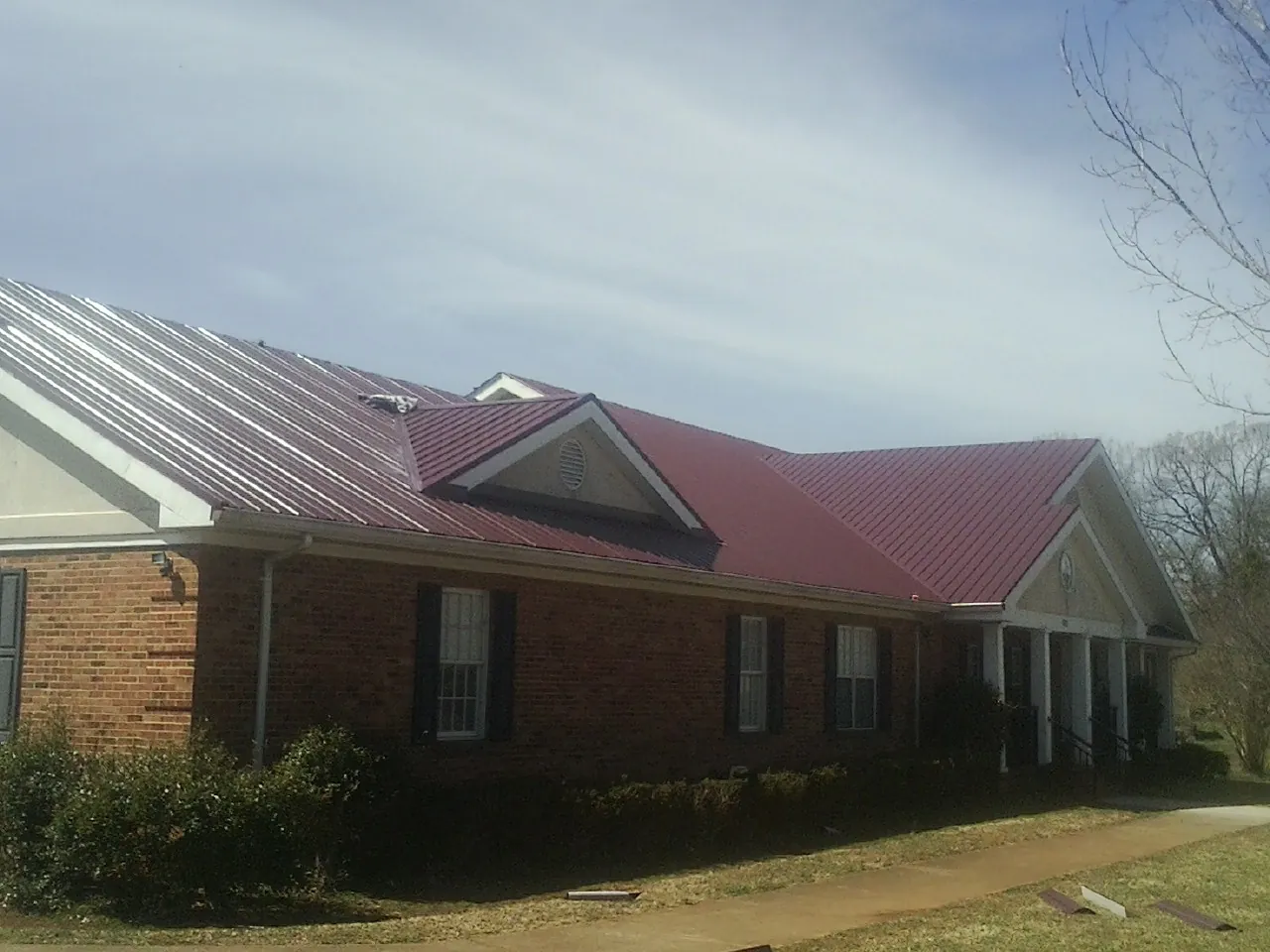 Red metal roof with gabled entries on a long brick building, from a Hail Damage Roof Repair job in Chichester