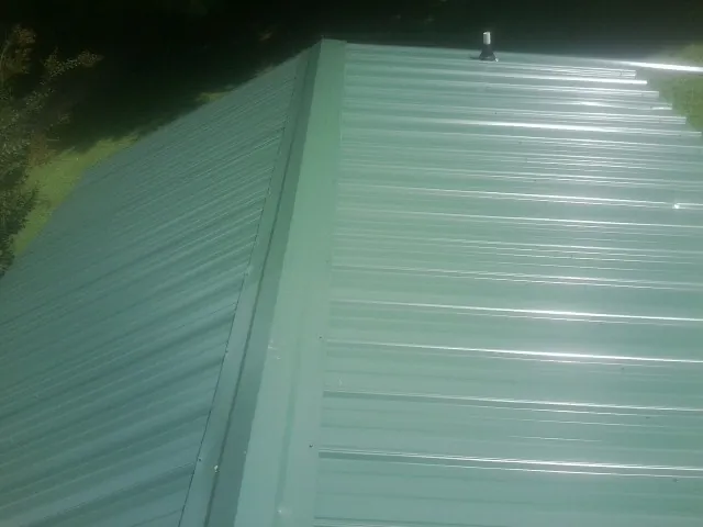 New green metal panels meeting at the ridge of a roof — Flat Roof Repair work by our crew in Chichester
