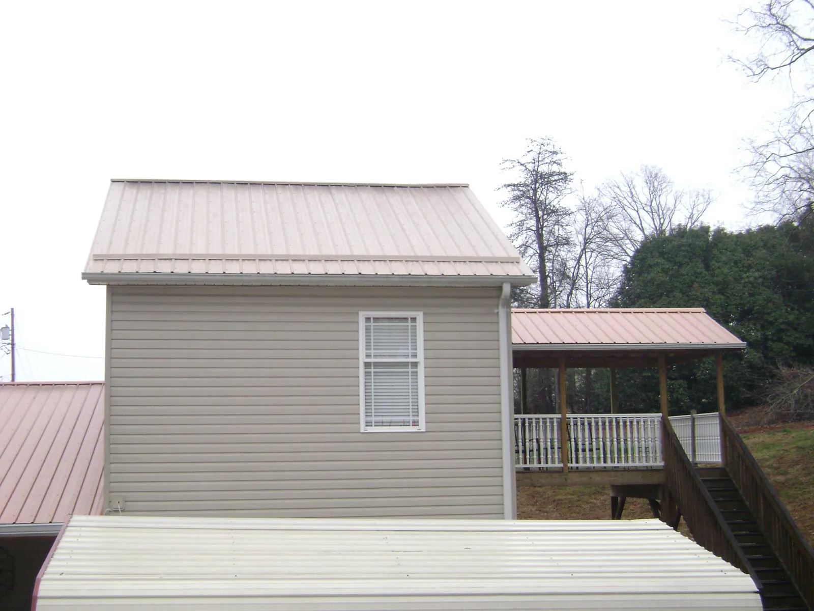 Tan metal roofs on a two story addition and attached porch, from a Roof Replacement job in Chichester